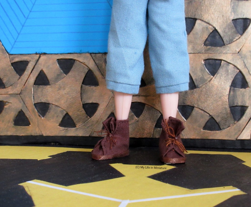 Shot shows Sarah's lower legs and feet, wearing Petra's brown shoes and three-quarter-length blue pants. She stands inside the TARDIS against one bronze-and-blue wall and on the black-and-yellow floor.