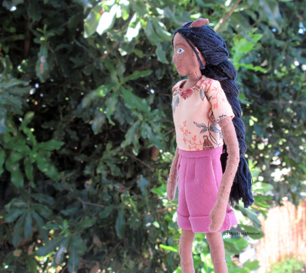 Petra walks right-to-left across the shot, hands swinging at her sides. She looks in the direction she's going, and is in front of the macadamia tree. 