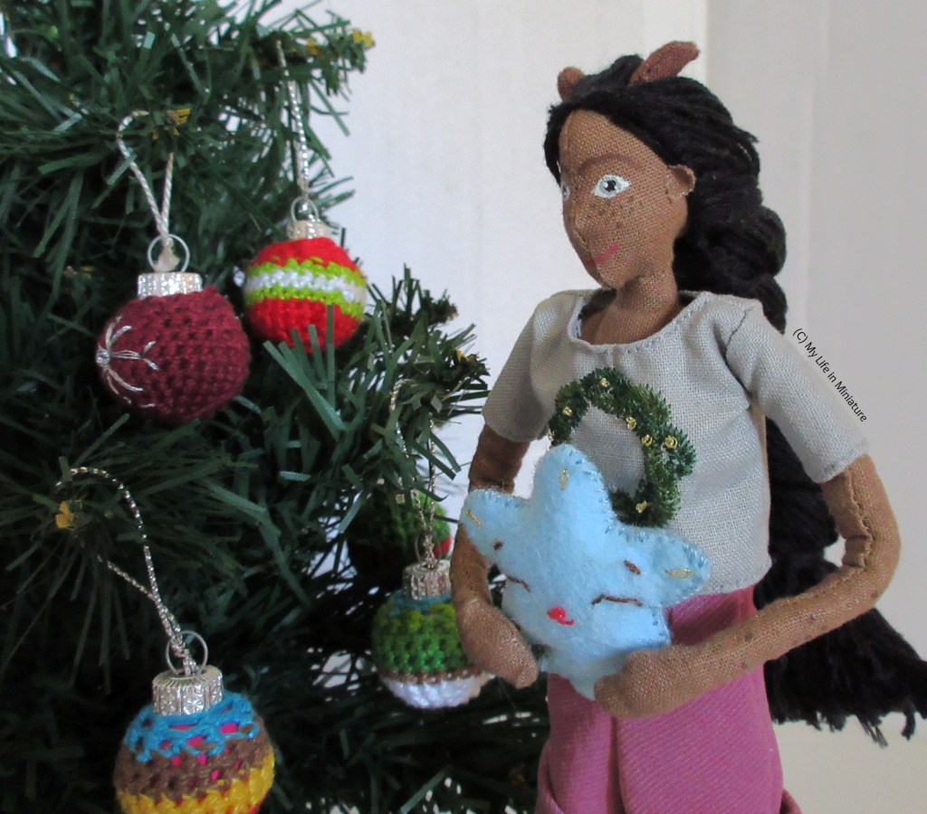 Petra stands to the right of the tree, holding a blue felt star. She is looking down at it as she faces to the left of the shot. 