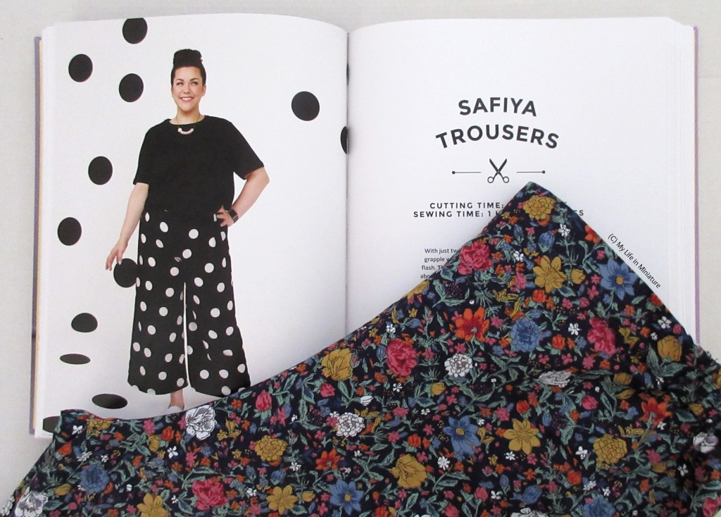 The floral pants are laid over an open book. The book is open to a double-page spread with an image of a model wearing wide-legged pants and 'Safiya Trousers'  written on the other page. 