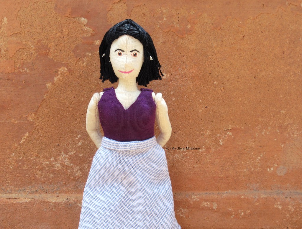 Tiffany stands outside against the terracotta backdrop, looking at the camera. She's wearing the purple jersey top with the blue-and-white skirt, hands behind her back.