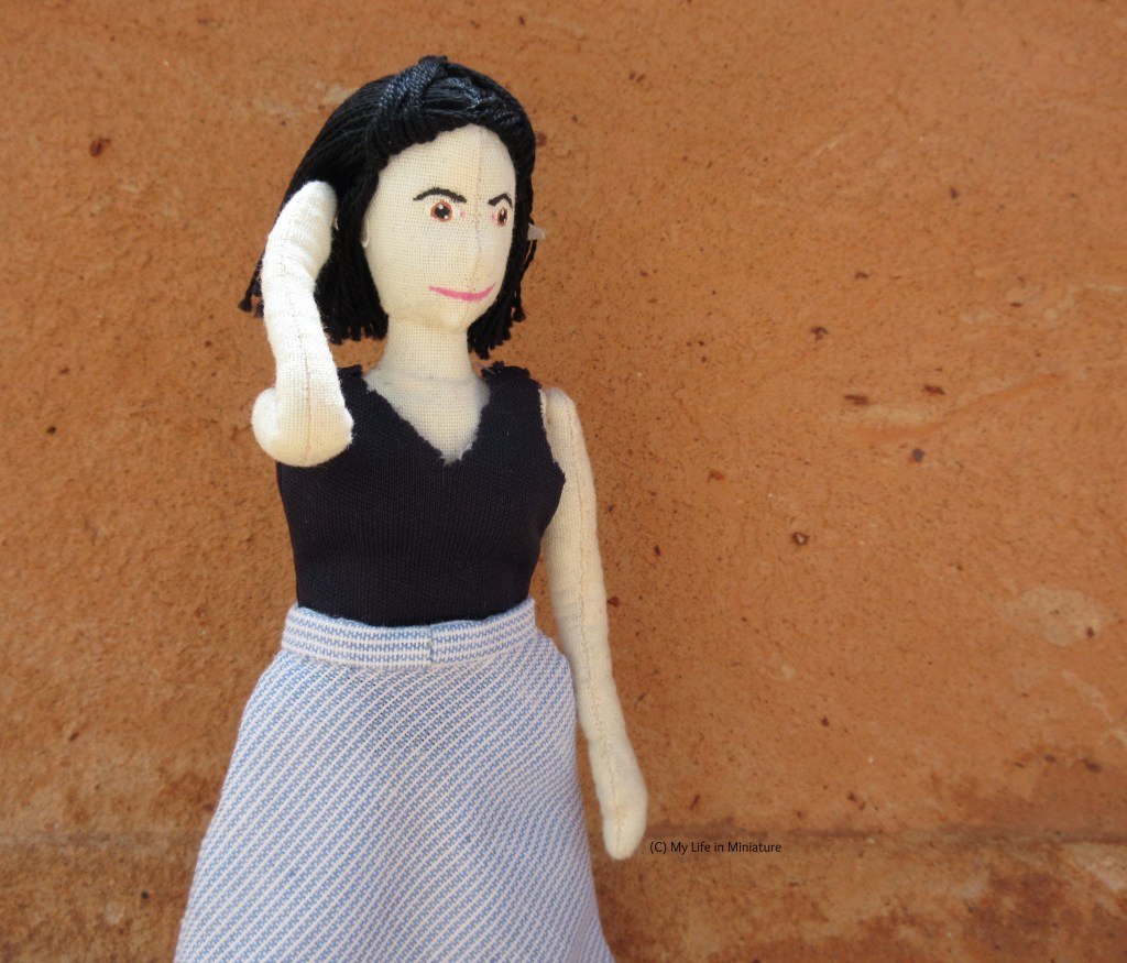 Tiffany stands against a terracotta backdrop, outside. She's wearing the navy jersey top with the blue-and-white skirt. She tucks some flyaway hairs behind her ear, looking to the right.