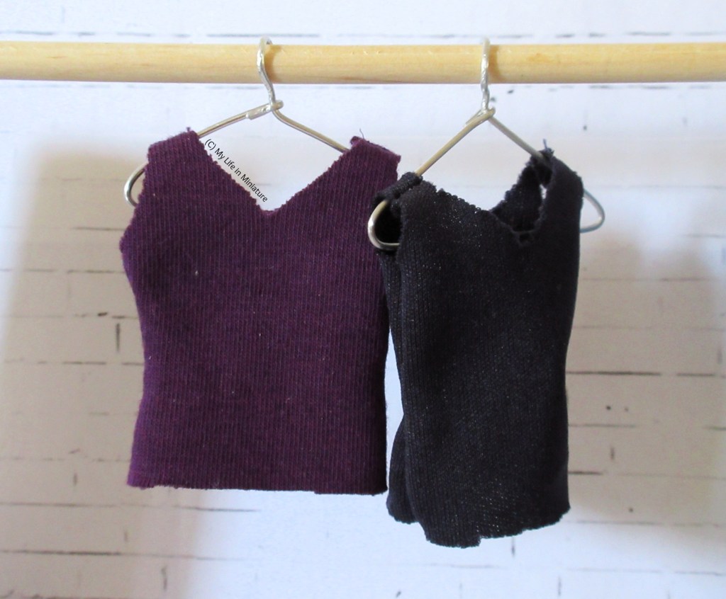 Two jersey singlets hang from coat hangers on a wooden pole. One is dark purple, one is navy.