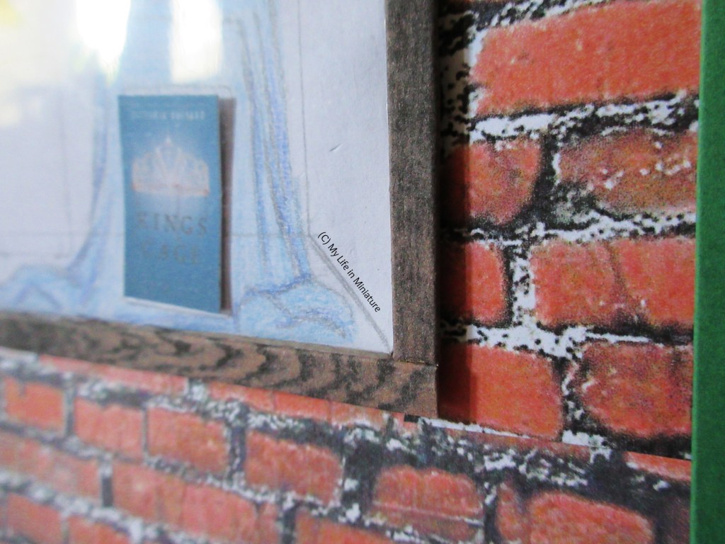 Close-up of the bottom-right of the window frame. The frame is dark wood, and is slightly elevated from the red brick. The corner of the display is also visible.