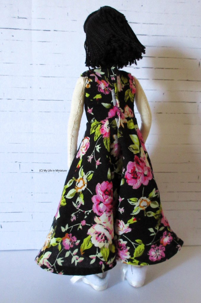 Tiffany faces away from the camera, wearing the ankle-length floral dress. The back of the dress is visible, and a Velcro fastening peeks out from the fabric overlap at the back of the torso.