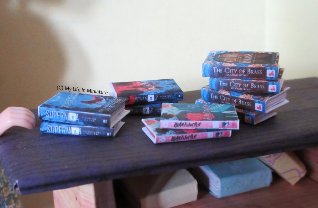 Several stacks of books are on the makeshift counter of The Palace Library, spines towards the camera. Three of the stacks have two books, and the one on the far right has four.