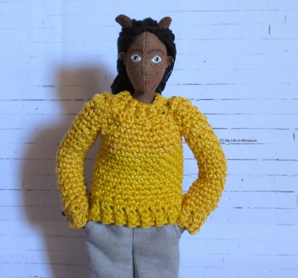 Petra wears a crocheted yellow jumper with ribbed cuffs and collar. She has her hands in her pockets and smiles at the camera. 
