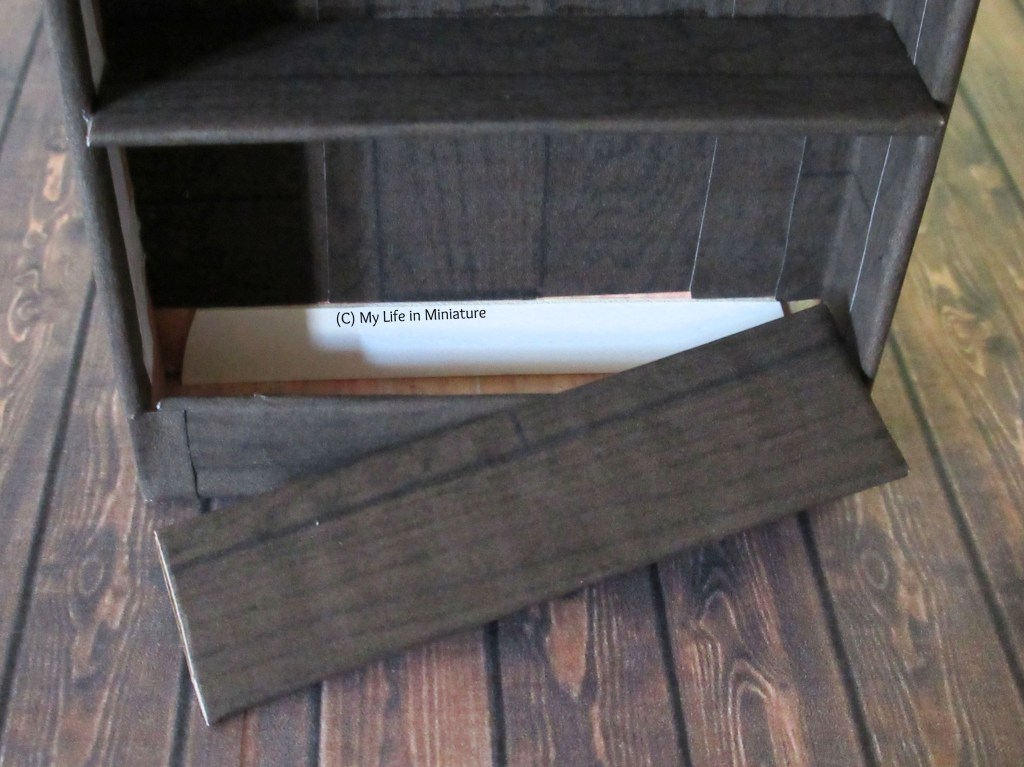Close-up of the bottom shelf of the counter's back, which is partly removed. Underneath the shelf is a small hollow space. 