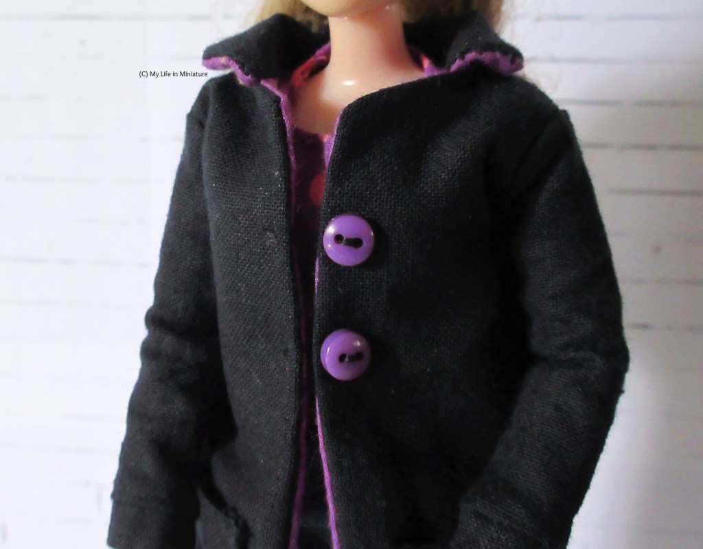 Close-up of the top front of the coat, with the buttons and collar clearly visible. The underside of the collar is in the same purple fabric as the lining.