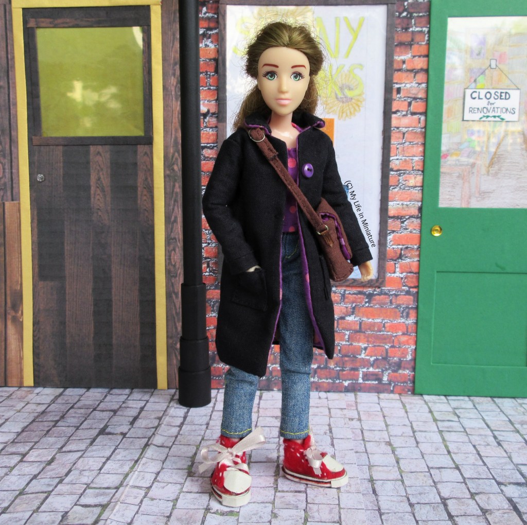 Sarah stands in front of The Palace Library, wearing her black coat and carrying her satchel. She has a hand in a coat pocket and smiles at the camera.