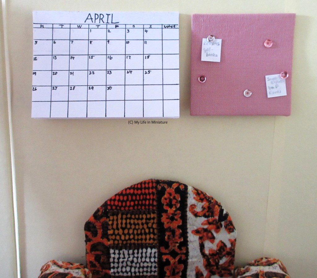 The patterned armchair sits against a wall in The Palace Library. Above it is a large calendar page, showing the month of April, and a small pink noticeboard. Both are attached to the wall.