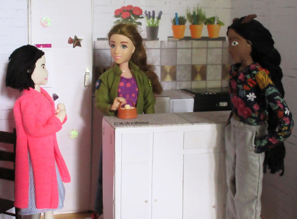 Sarah, Tiffany and Petra stand in Sarah's kitchen. Sarah is behind the island, hand on the handle of a basket of plain eggs. Tiffany is to the left, hands clasped, talking to Sarah. Petra is to the right, looking past Tiffany to the table.