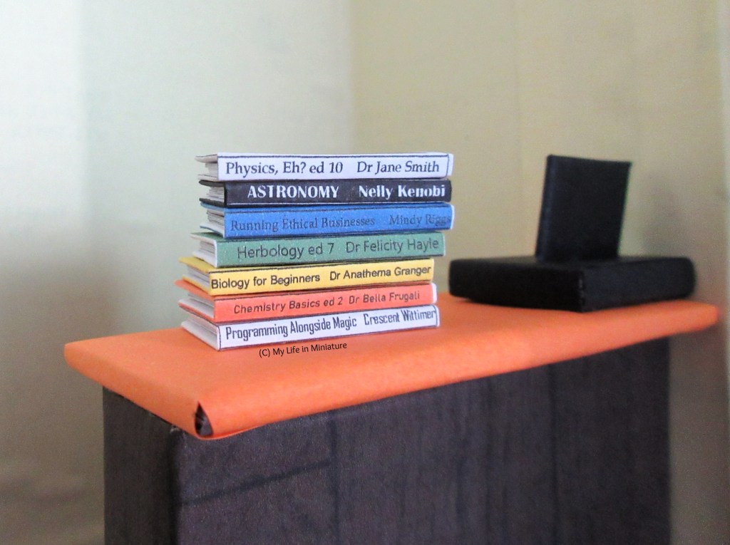 A stack of textbooks sits on the front counter of the Palace Library. They are for topics like physics, astronomy, business, herbology, biology, chemistry, and programming.