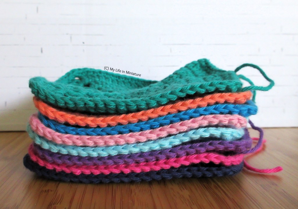 The eight crochet squares are stacked and photographed from the side against a white brick background. 