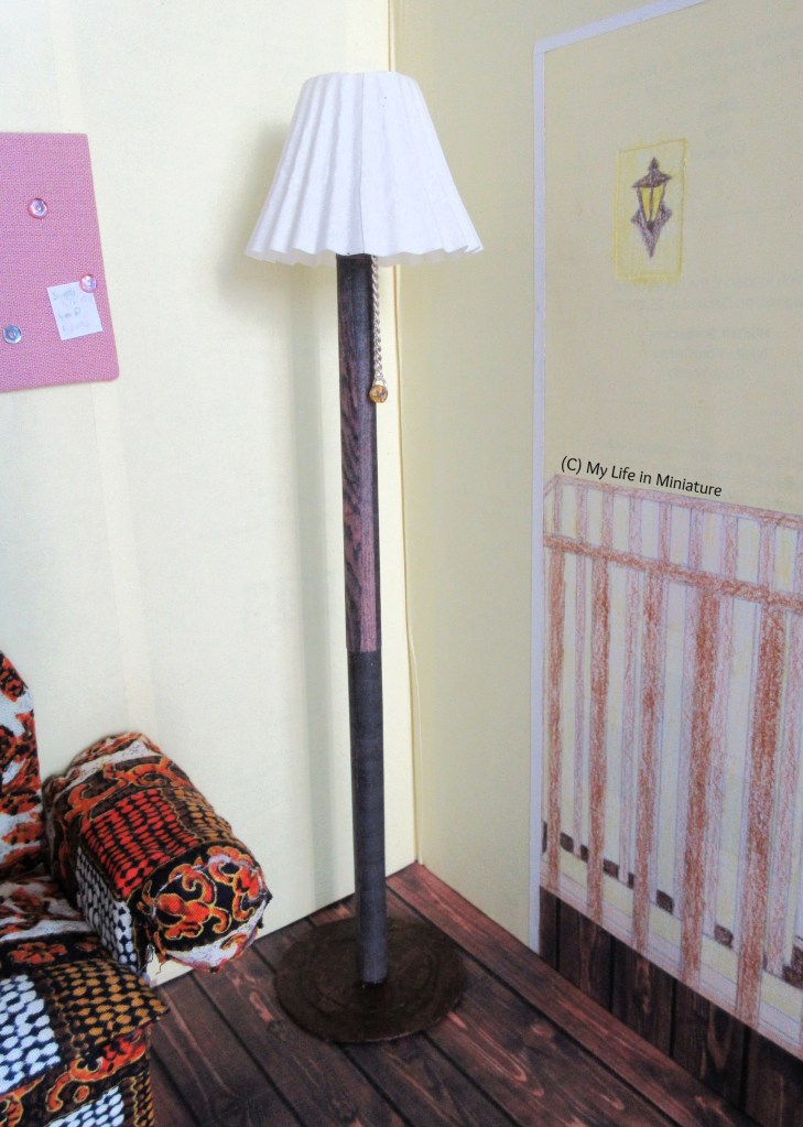Close-up shot of the freestanding floor light. The base and pole (?) looks like dark wood, there is a concertina'd white lampshade, and a small silver chain hangs from beneath the shade. 
