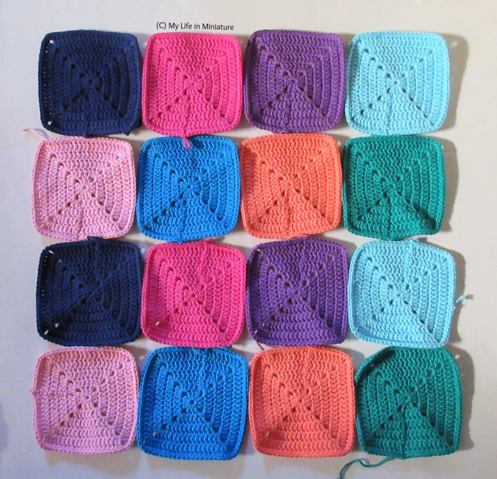 Sixteen squares of crochet are laid out on a white background. The first row's colours are (left to right) navy, pink, purple, and pale blue. The second row's colours are (left to right) pale pink, blue, peach, and green. The two rows are repeated in the third and fourth rows respectively.