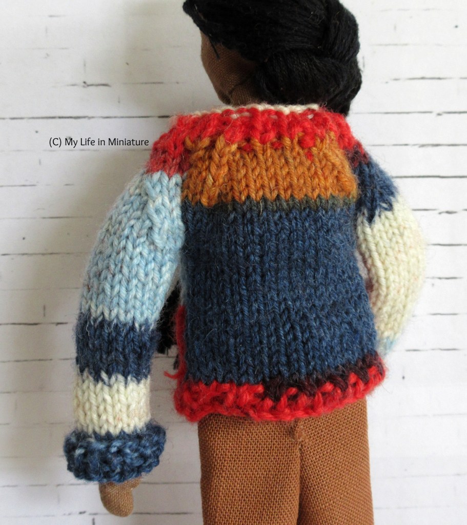 Petra has her back to the camera and her hair over her shoulder, showing the back panel of the multi-coloured jumper. The back panel is red, dark blue, and light brown. 