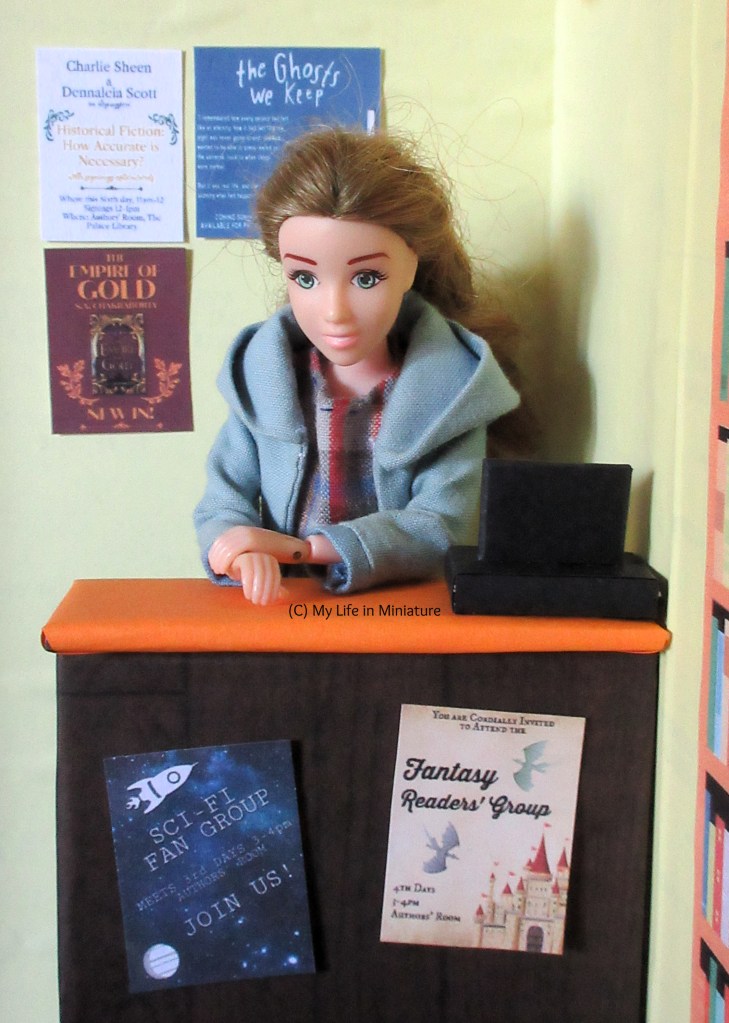 Sarah stands at the counter of The Palace Library. Three flyers are on the wall behind her, and she leans over the counter to look over it. On the front of the counter are the two other flyers.