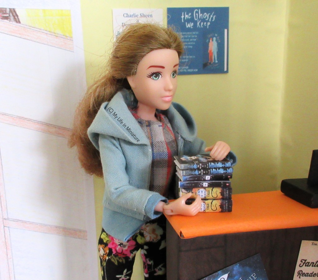 Sarah eases the stacked six books off the Palace Library's counter and into her arms. She looks down at the books, and is wearing a blue hoodie and floral pants.