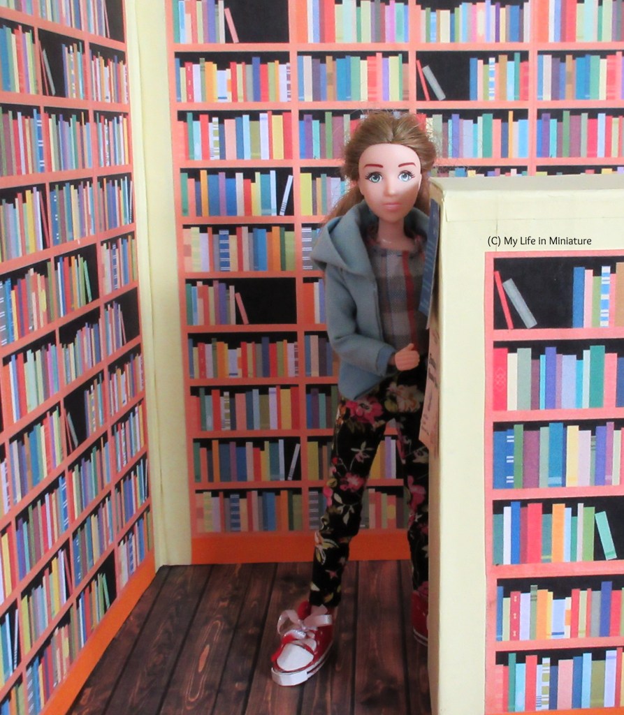 Sarah leans out from behind the end of an aisle in the Palace Library. She is surrounded on all sides by bookshelves full of books. Some flyers are on the end of the aisle, which goes up to about Sarah's eyes in height.