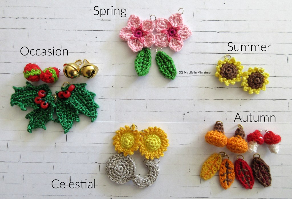 22 crocheted objects (and two gold bells) sit on a white brick background, arranged into five categories. Clockwise from the top is spring, summer, autumn, celestial, and occasion. The spring category has two green leaves, and two cherry blossom flowers. The summer category has two sunflowers. The autumn category has two pumpkins, two red-topped mushrooms, and four leaves in shades of yellow, orange, red, and brown. The celestial category has two suns, and a full and crescent moon in silver. The occasion category has the two gold bells, two baubles, and two bunches of holly. 