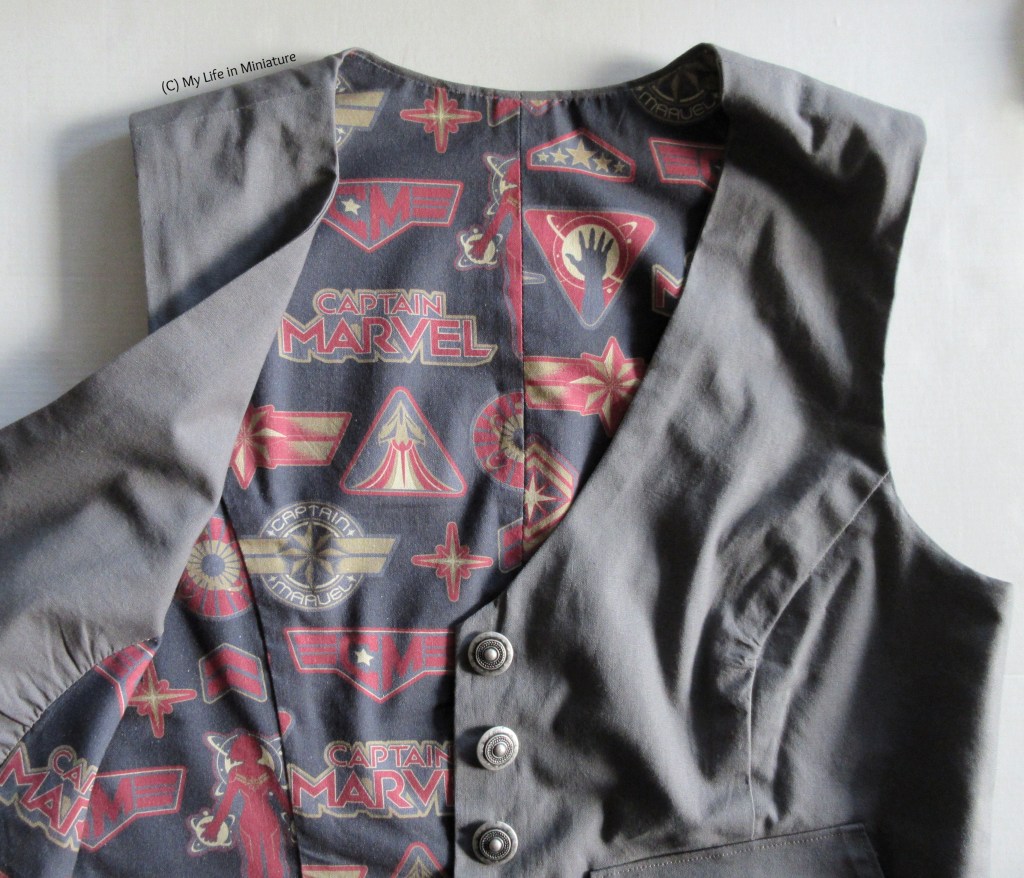 The grey waistcoat is laid out on a white background. One side of the front is open to reveal the lining, which is Captain Marvel fabric. 