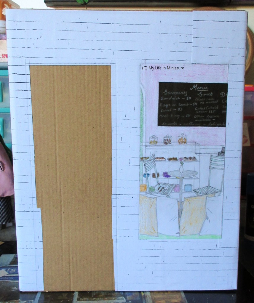 The front of a cereal box fills the image, covered in cardboard that peeks out from behind white brick paper. A rectangle for the door is left uncovered on the left of the box, and a view into the shop is on the right. 'Inside' the shop is cushions on a window seat in the foreground, a table and chairs in the midground, and a counter filled with desserts in the background. On the wall in the very back is a chalkboard menu. 