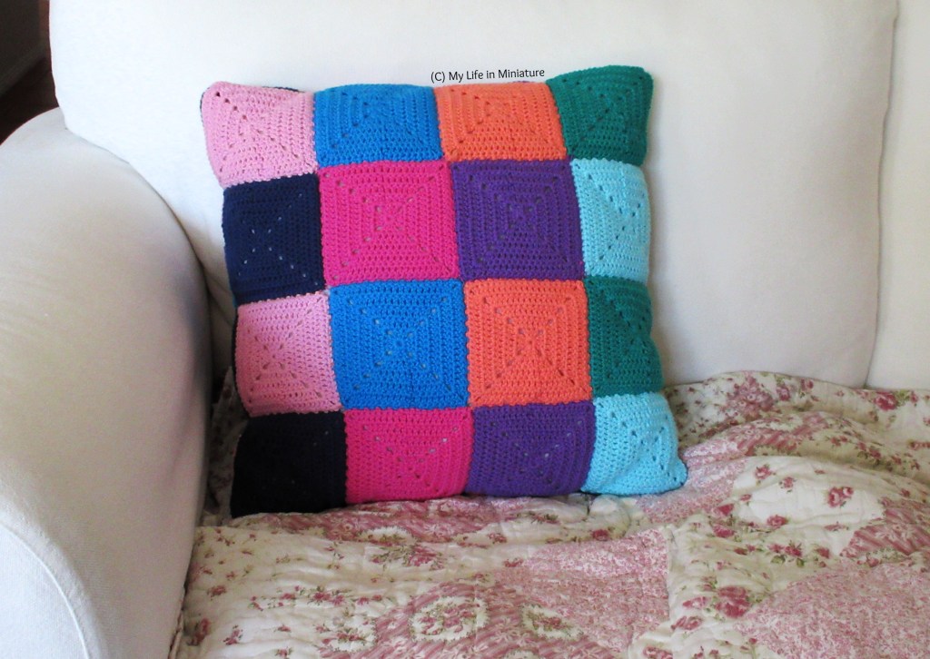 The back of the crocheted cushion cover sits on a white couch. There are no buttons or buttonhole additions to overlap any squares, so a grid of 4x4 squares is visible.