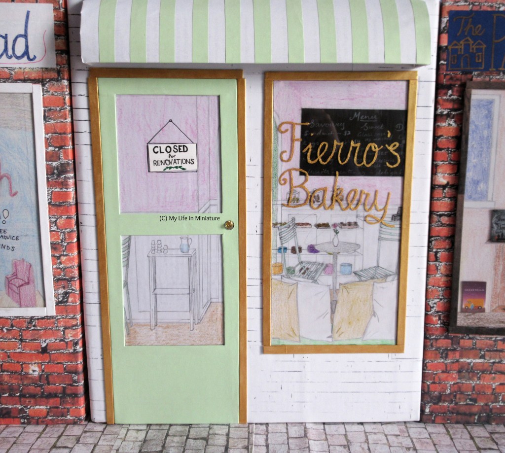 The storefront for Fierro's Bakery is pictured, in-between Needle and Thread and the Palace Library. The name of the bakery is painted on the window in gold, and a green door is to the left. Gold borders the door and window, and the store has a white brick background and a white-and-green striped awning across the top of the storefront.