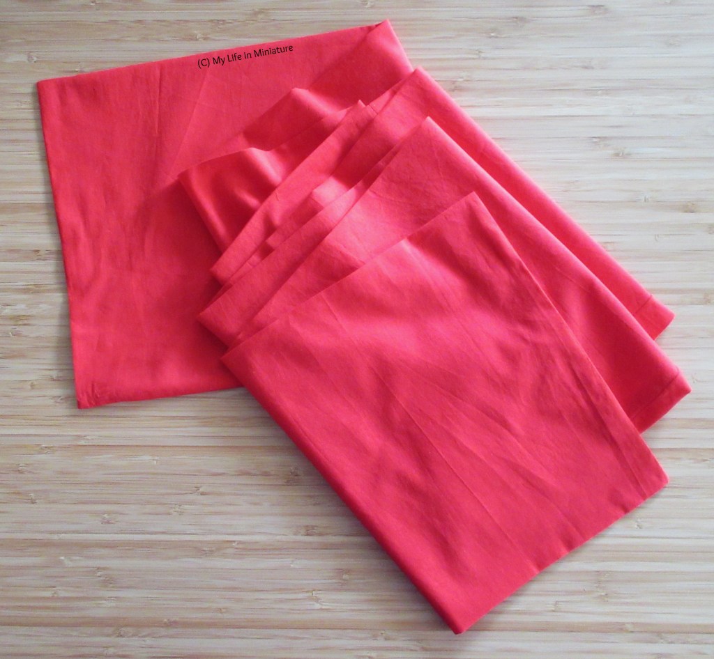 A long rectangular strip of bright red fabric sits, loosely folded accordion-style, on a wood background. 