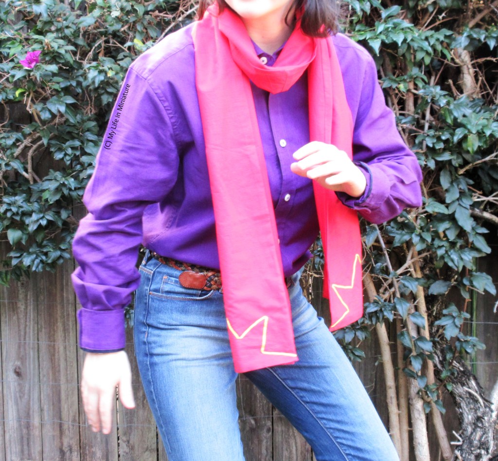 The author stands in front of a hedge, wearing the red scarf looped around her neck so both ends are in front. She also wears a purple button-down shirt tucked into jeans. She half-crouches and has one arm up, like she's heard a noise and is about to make a superhero's exit. 