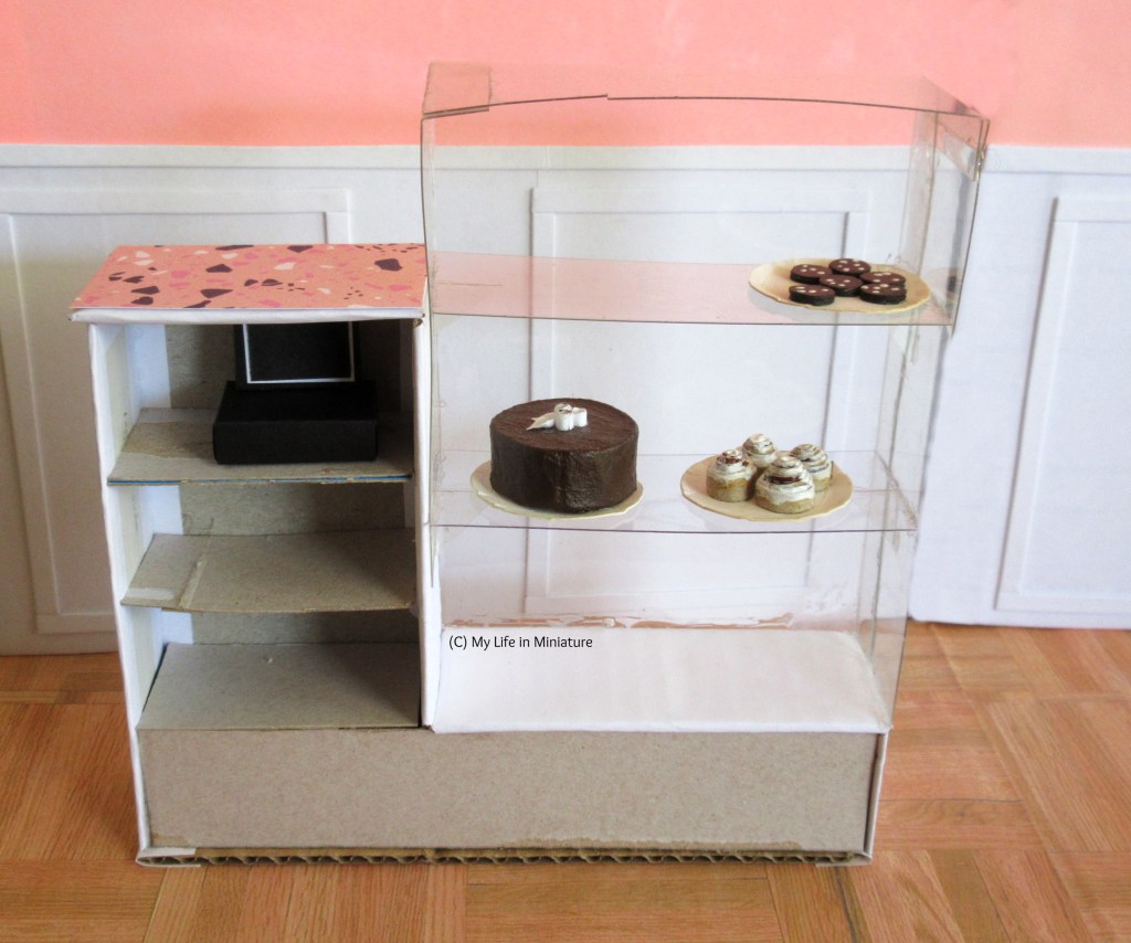Image shows the back view of the front counter. To the right is the glass cabinet, which does not have a back for easy access. The left side under the cash register bit has three shelves, one of which now holds the cash register.