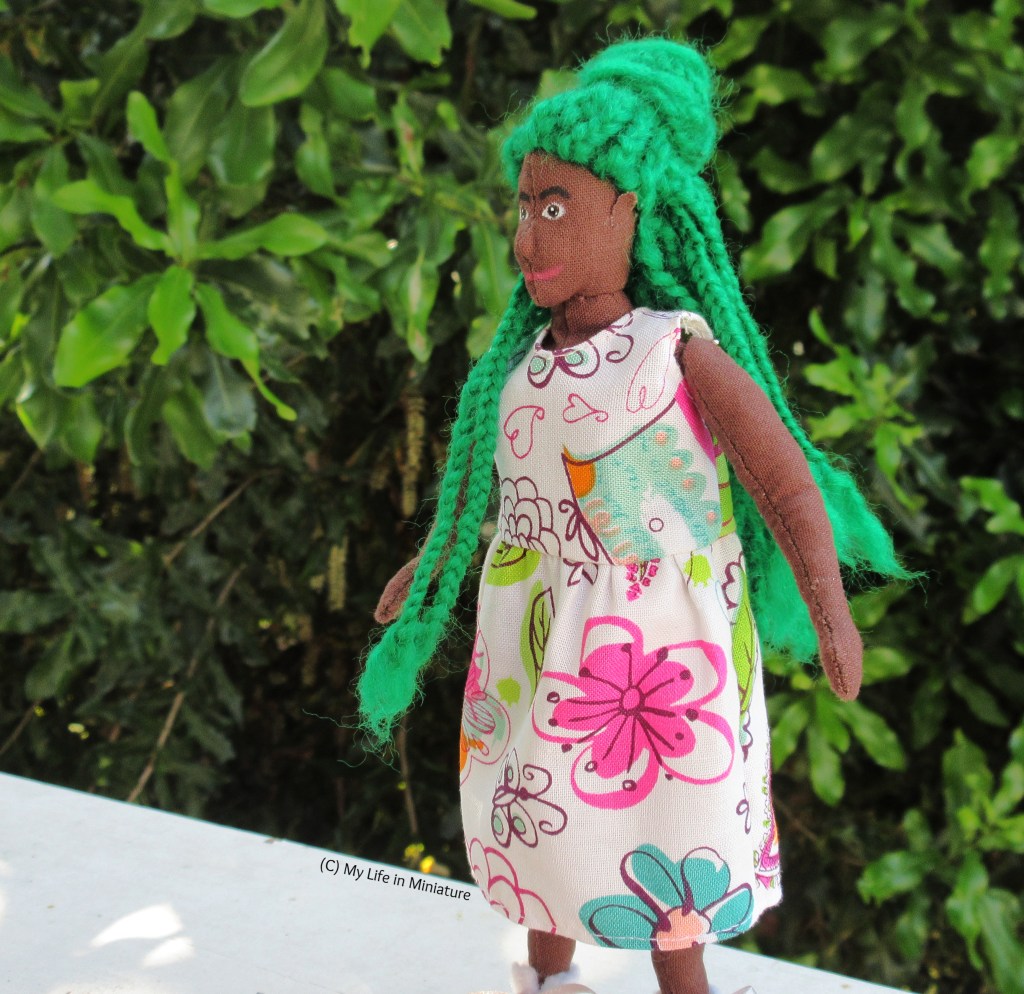 Hazel stands in front of a green leafy bush on a white wood surface. She is facing left, captured in the motion of twirling on the spot to fan out the skirt of her dress, princess-style. Her braids swing with the motion, and her hands are out to the sides. 