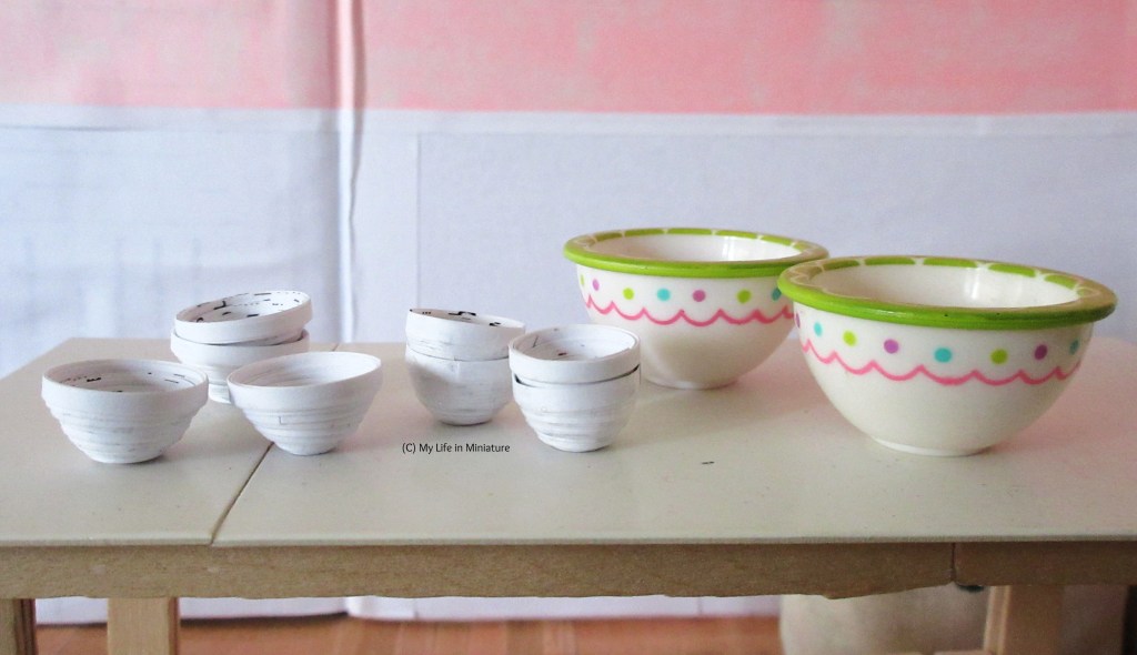 Close-up of the bowls on the work bench. Two of them are very big, with green rims and pink decoration on the outside. The other eight are white with black freckles inside; four are medium-ish sized, and four are quite small. 