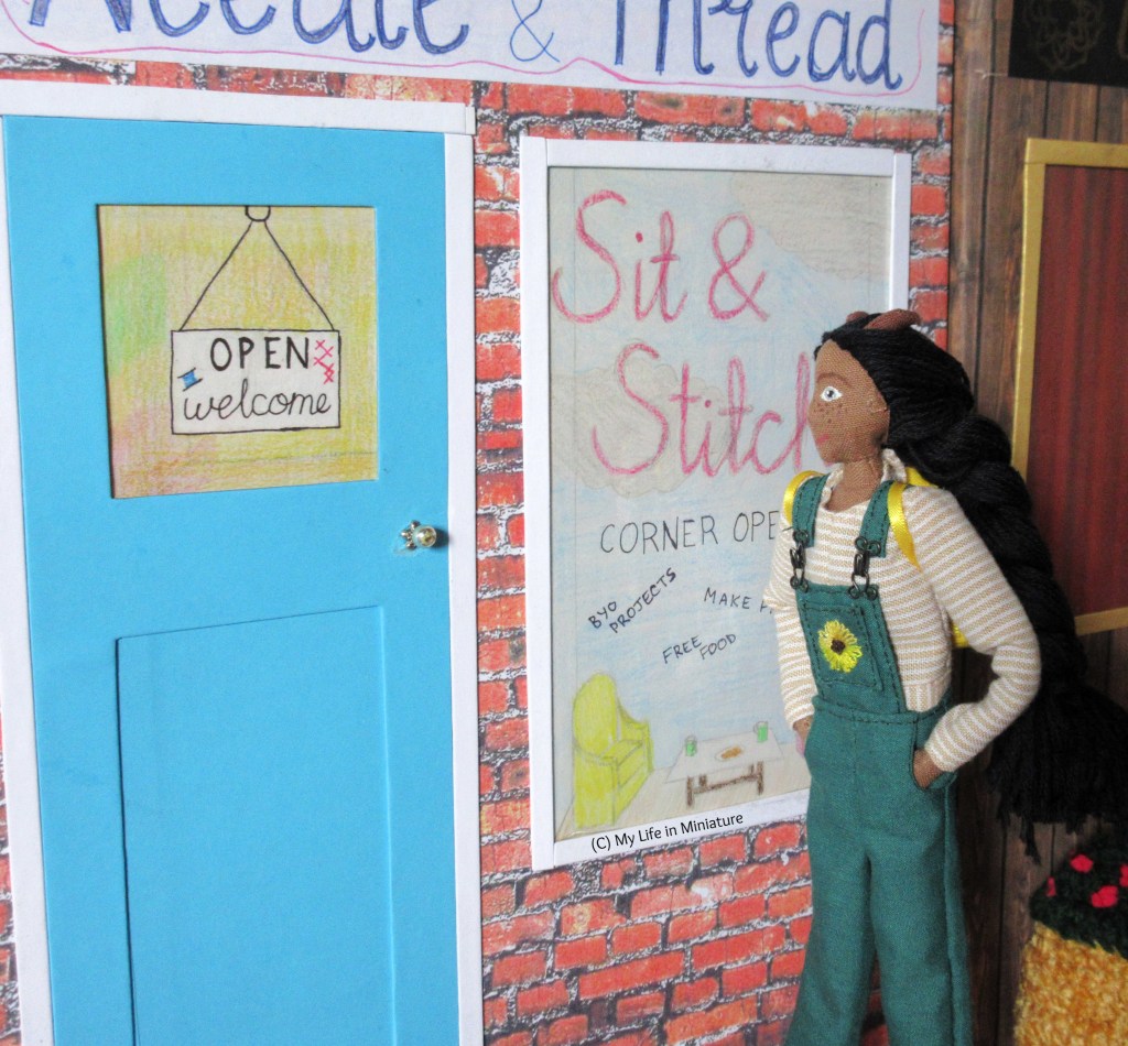 Petra walks towards the blue front door of Needle & Thread, hands in pockets with a smile on her face. She wears a beige striped long-sleeves shirt with green dungarees. Her yellow backpack is on her back. She looks at the window display as she passes. 