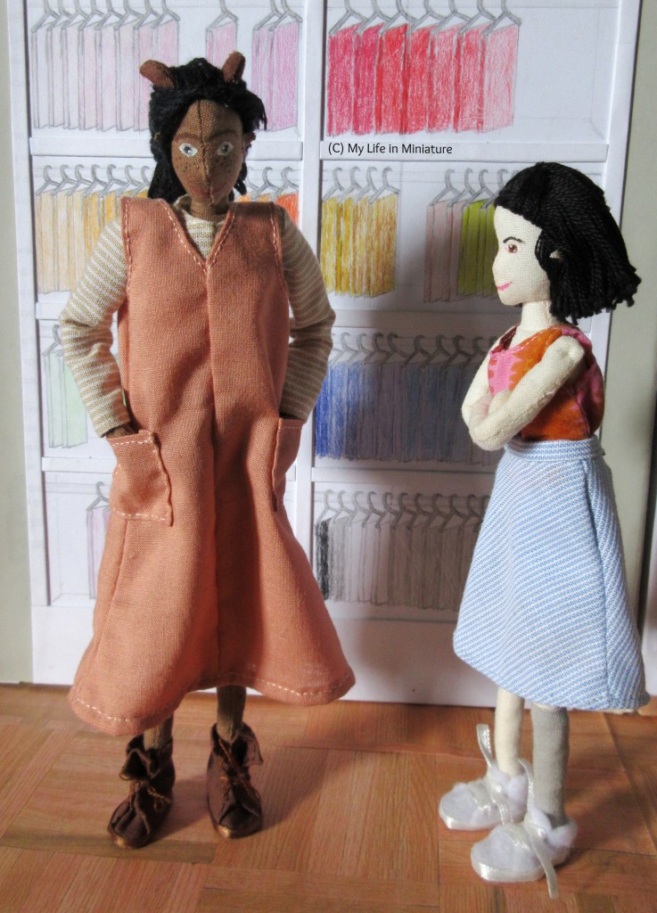 Petra and Tiffany stand side by side in front of Needle & Thread's fat quarters. Petra is testing the patch pockets of her new peach dress, while Tiffany stands to the side, watching with her arms crossed.