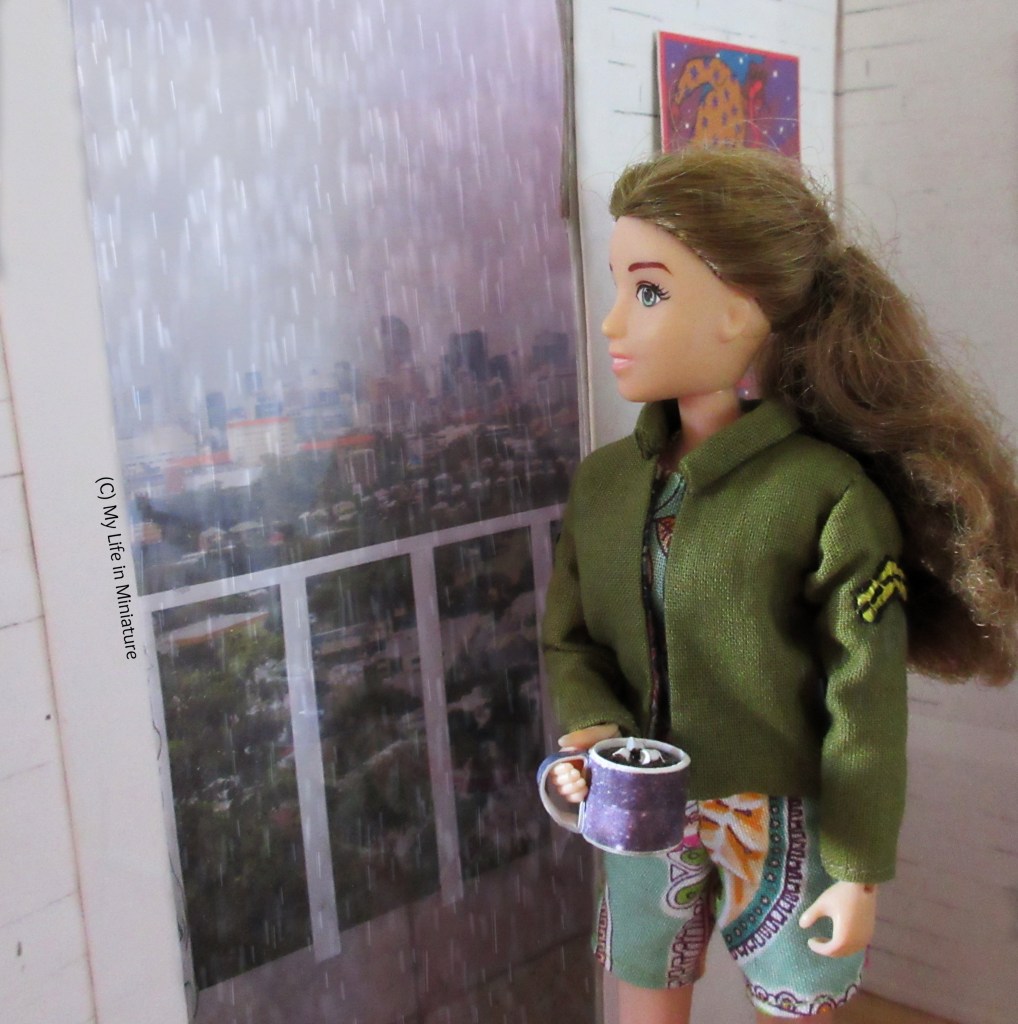 Sarah stands at a window in her apartment, a mug of hot chocolate in her hand. She wears the khaki jacket and playsuit combo, and is looking out at the rather heavy rain falling outside. Her view looks out over a city, with a balcony in the foreground. Behind her are white brick walls, and behind her head is a bright piece of art.