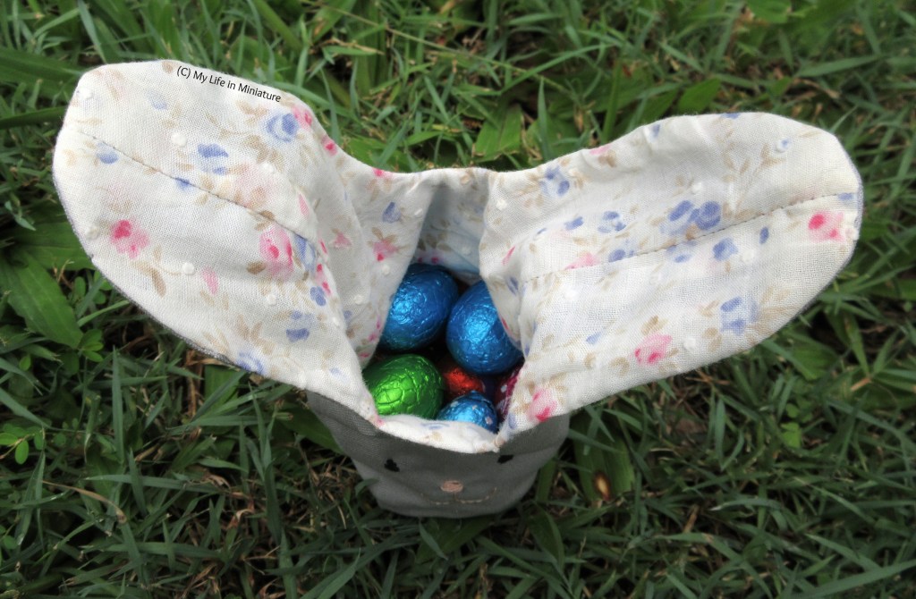 The rabbit bag, photographed from above, untied. The floral fabric on the inside of the ears extends to the lining of the bag. You can also see chocolate eggs inside the bag. 