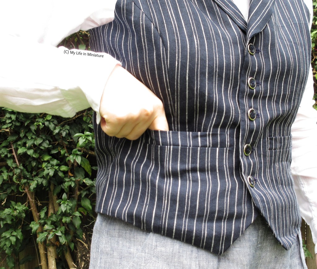 Close-up of the pinstriped waistcoat, specifically one of the single welt pockets. The author's fingers are tucked into it, to illustrate how it opens. Also visible are the five buttons down the front of the waistcoat, which are navy blue with silver around the outside.