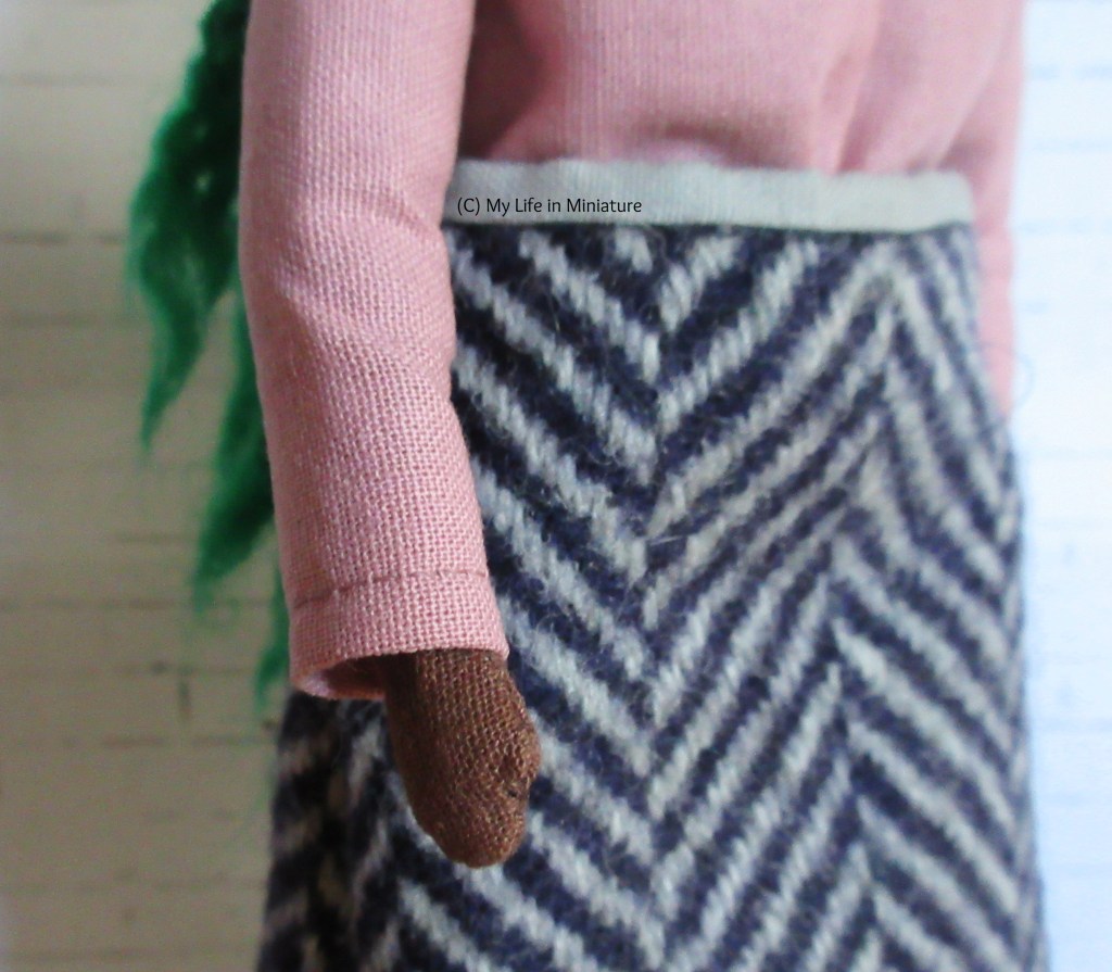 Close-up of the sleeve of Hazel's top as Hazel's arm hangs beside her. It's hemmed at the wrist, and most of the background is Hazel's skirt.