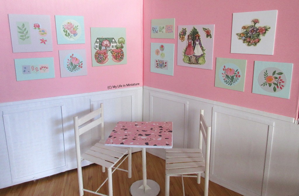 Wide-angle shot of one corner of Fierro's dining area. Two walls area visible with a dining table and chairs in front. The walls have pastel canvases mounted on them, in various shades, sizes and shapes. All have floral art (in the form of stickers) on them.