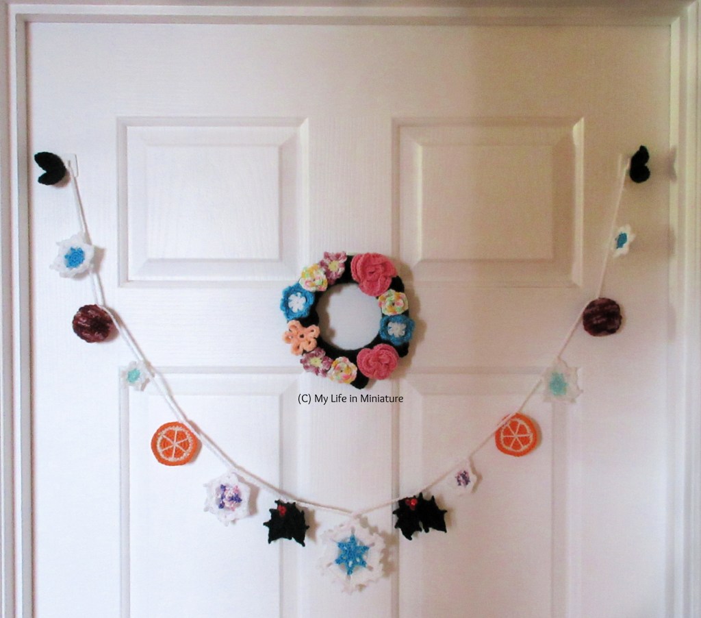 The wintery garland hangs on a white door from two hooks in the top corners of the door. A small crochet floral wreath sits above the central snowflake of the garland.