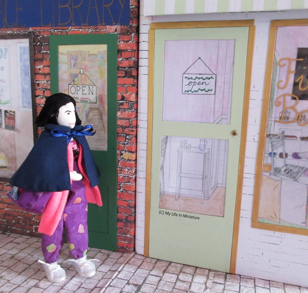 Tiffany walks towards the front door of Fierro's, looking up at the sign. She wears purple pants with a bright pink cardigan and a navy cape over the top. Under the cape, she has her dark purple tote over her shoulder. 