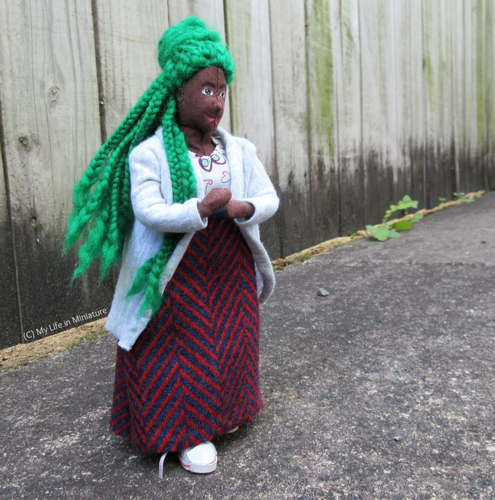 Hazel walks past the camera in her new wool skirt, braids and skirt lifting in the wind. The background is the same wooden fence, with some weeds growing at the base in the distance.