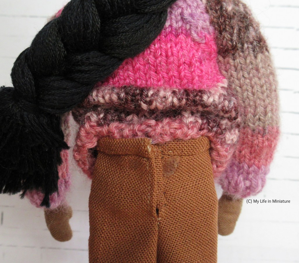 Close-up of the back closure of the brown pants, as Petra wears them with a pink knitted jumper. The edge of a placket in the same fabric can be seen, as well as the glue mark where the velcro used to be.