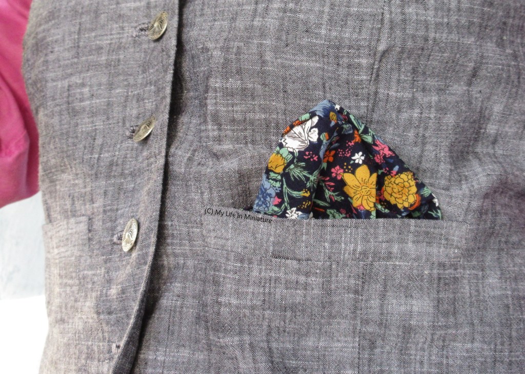 Close-up of one of the welt pockets on the grey waistcoat. The floral lining has been pulled out of the pocket in a triangle, so it stands out against the plain fabric. 