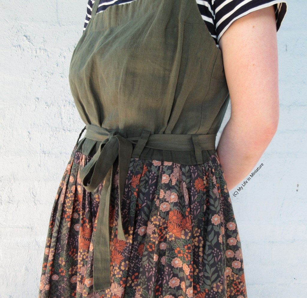 Close-up of the waist area of the pinafore. The skirt portion is pleated into the bodice, which has been lengthened and had belt loops added. The tie is the same one from the dungarees, which is threaded thorough the belt loops and tied in an off-centre bow. 