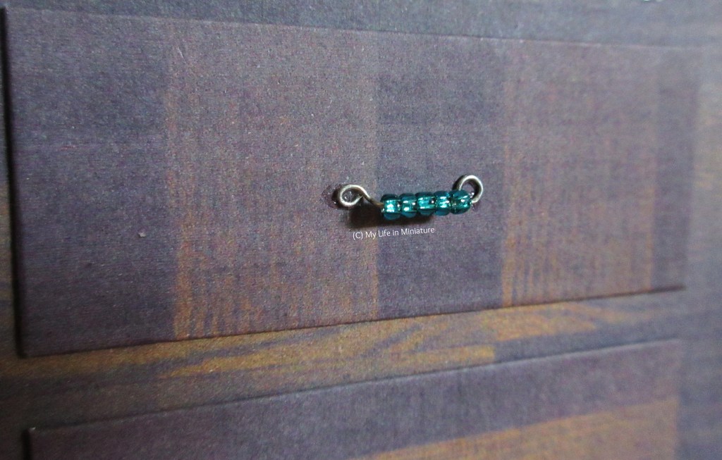 Close-up of one of the drawer handles. It's made of wire, and has five turquoise beads across the centre. The two ends are circles glued onto the drawer front.