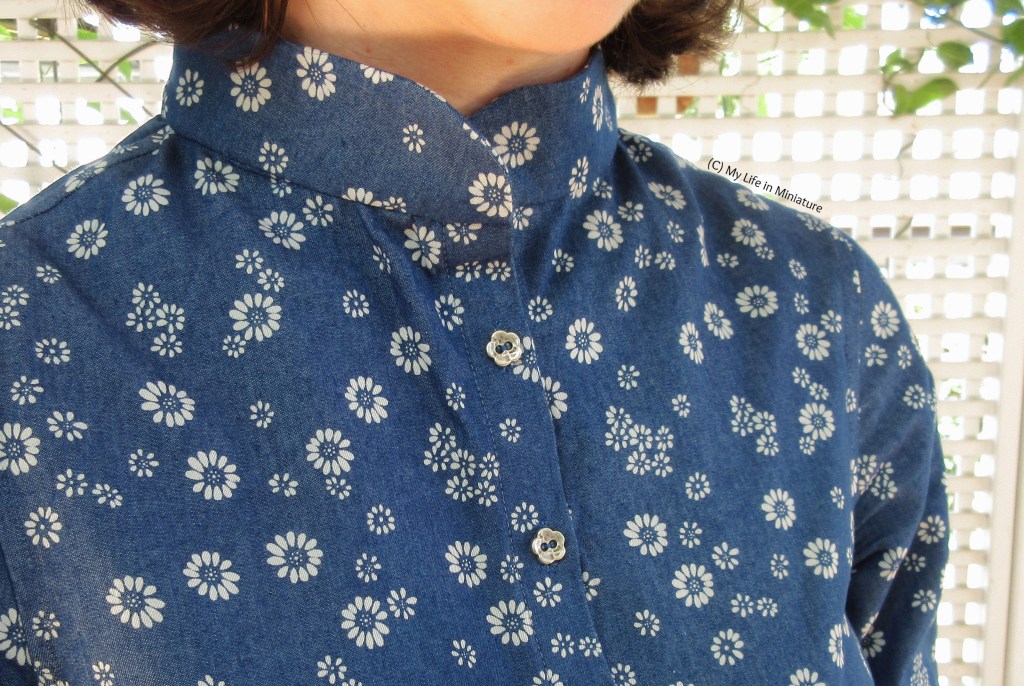 Close-up of the dress' collar area. The collar itself has rounded corners, and the buttons are small silver flower shapes. 