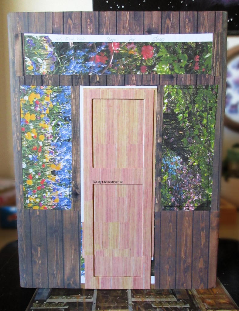 The same dark wood storefront, this time with a paler wood door in the centre. The door has no doorhandle yet, or frame. 